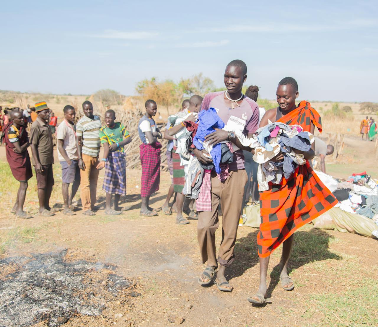 services-01 Local community members participate in a clothing distribution event under sunny skies in a rural setting.